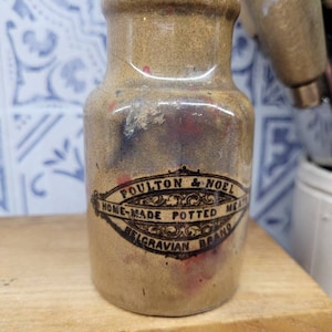 May include: A brown ceramic jar with a black and white label that reads "Poulton & Noel Home-Made Potted Meats Belgravian Brand".