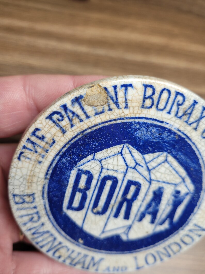 May include: A vintage ceramic lid with a blue and white design. The lid features the text "The Patent Borax Birmingham and London" and a blue and white image of the word "Borax" in a geometric shape.
