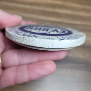 May include: A white ceramic lid with blue lettering that reads "Borax" and "The 20 Mule Team" with a cracked surface.
