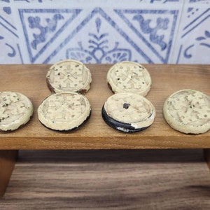 May include: Six round, cream-colored ceramic tiles with a black border and a decorative pattern in the center. The tiles are arranged in two rows of three on a wooden surface.
