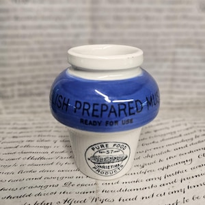 May include: A small white and blue ceramic jar with a rounded body and a narrow neck. The blue section features the text "LISH PREPARED MUS" and "READY FOR USE". The white base displays a black "HEINZ PURE FOOD PRODUCTS" logo with "57".