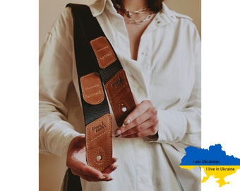 May include: Black and brown guitar strap with leather detailing. The strap features a black woven section with brown leather patches and a metal button. The brand name "Stages Audio" is visible on the leather patches.