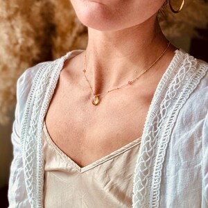 Op de afbeelding: Een gouden ketting met een traanvormige hanger van een gele edelsteen en kleine, gelijkmatig verdeelde edelstenen langs de ketting.