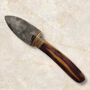 May include: A gray flint knife with a wooden handle wrapped in brown leather. The handle has a dark brown wood grain.