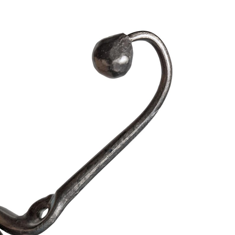 May include: A dark gray, hand-forged metal wall hook featuring a curved, slender arm that terminates in a rounded, textured knob. The base of the hook includes a visible mounting hole, and the entire piece displays a rustic, hammered finish.