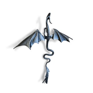 May include: A black metal dragon sculpture with wings outstretched and a long, curled tail. The dragon is in a flying pose, with its head tilted upwards.