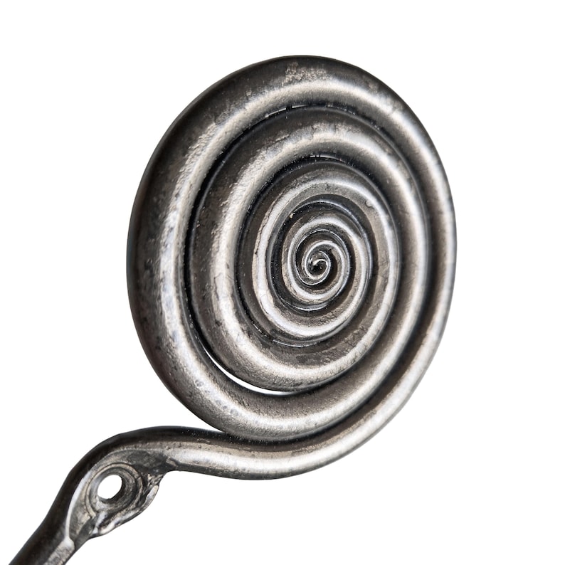 May include: A dark silver-toned metal wall hook featuring a prominent circular spiral design at the top. The hook has a textured, weathered finish and includes a single circular mounting hole at the base of the spiral for attachment to a surface.