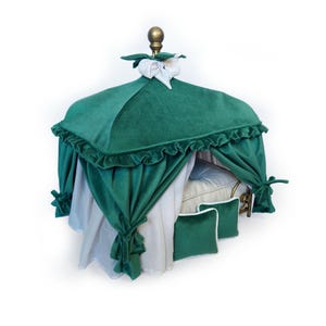 Puede incluir: Una lujosa cama para mascotas de terciopelo verde con dosel. La cama presenta un remate dorado, cortinas blancas y almohadas verdes a juego. El dosel está adornado con un borde con volantes. La cama está diseñada para mascotas pequeñas.