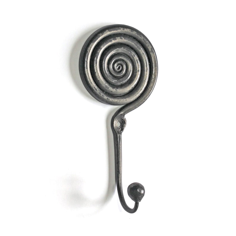 May include: A dark gray metal wall hook featuring a circular spiral design at the top and a curved hook ending in a small spherical knob. The piece includes a single mounting hole located just below the spiral section for attachment.