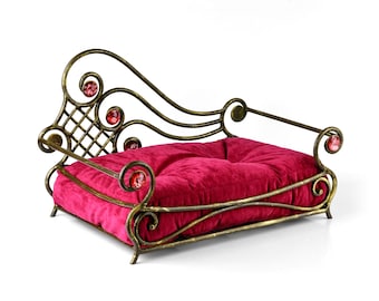 Può includere: Un letto per cani in metallo dorato con un cuscino in velluto rosso. Il letto ha un design decorativo e ornato con volute e un motivo a rombi. Il letto è decorato con gemme di vetro rosso.