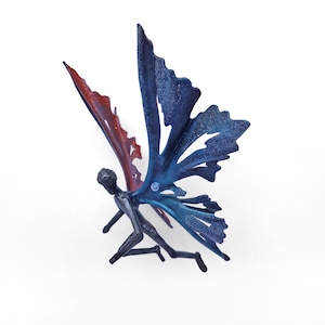 Puede incluir: Una escultura de metal de un hada con alas azules y rojas. El hada está en vuelo con las alas extendidas. La escultura está hecha de metal y tiene un acabado rústico.