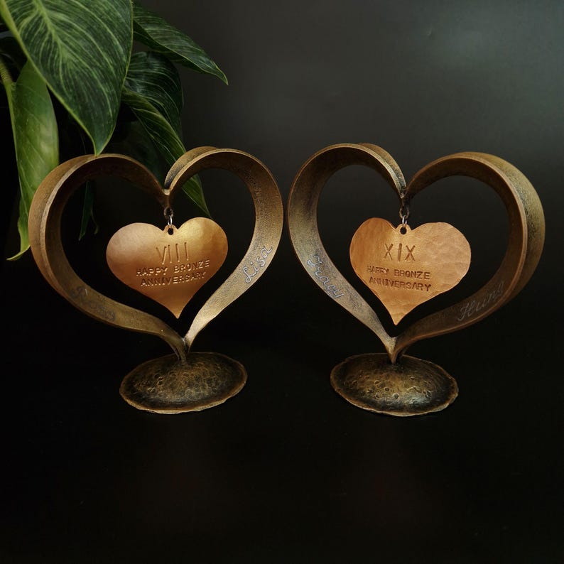 Puede incluir: Dos esculturas en forma de coraz&oacute;n de bronce con un colgante de coraz&oacute;n de cobre martillado. Los colgantes dicen "VIII Happy Bronze Anniversary" y "XIX Happy Bronze Anniversary". Las esculturas tienen un acabado texturizado.