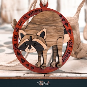 Finished multi wood raccoon ornament hanging from a ribbon, masked face and striped tail in different wood tones.