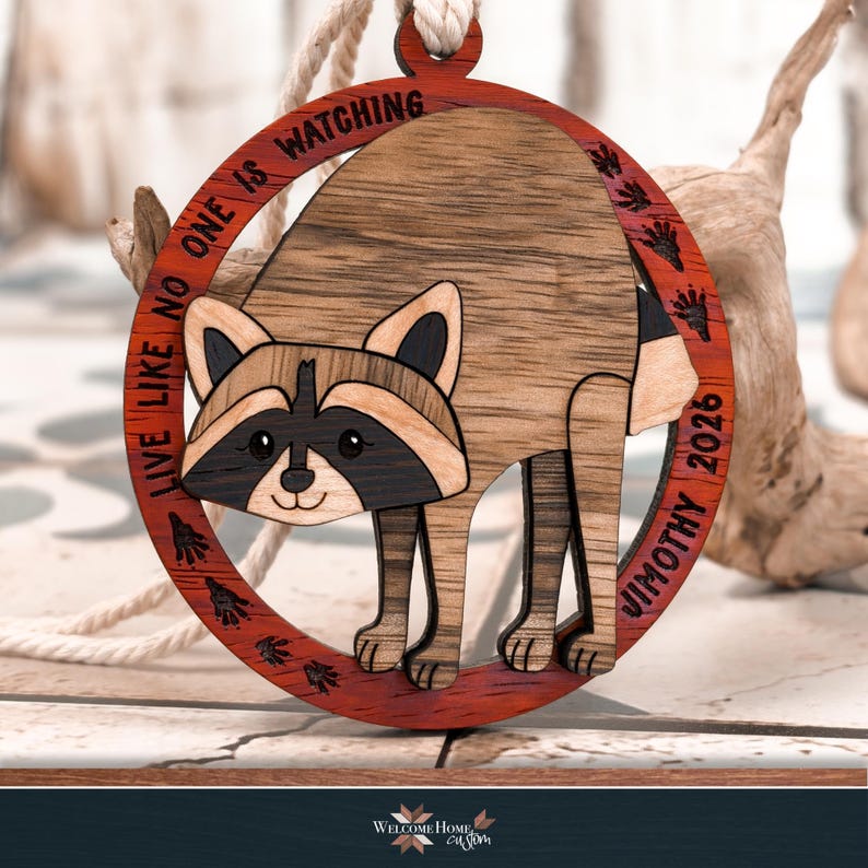 Finished multi wood raccoon ornament hanging from a ribbon, masked face and striped tail in different wood tones.