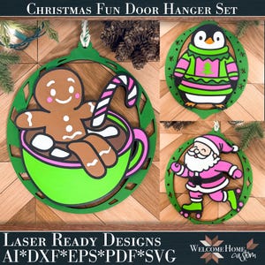 Puede incluir: Un conjunto de tres colgadores de puerta con temática navideña. Uno presenta un hombre de jengibre en una taza, otro un pingüino con un suéter y el último, Papá Noel sobre patines. En verde, marrón, rosa y blanco. Texto: "CHRISTMAS FUN DOOR HANGER SET".