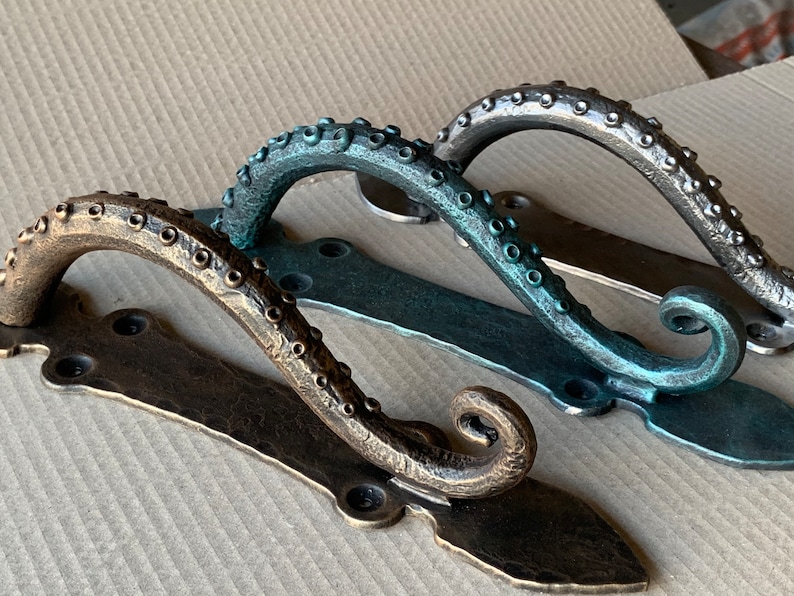 May include: Three octopus-shaped door handles with a textured finish. The handles are in different colors: bronze, teal, and silver.