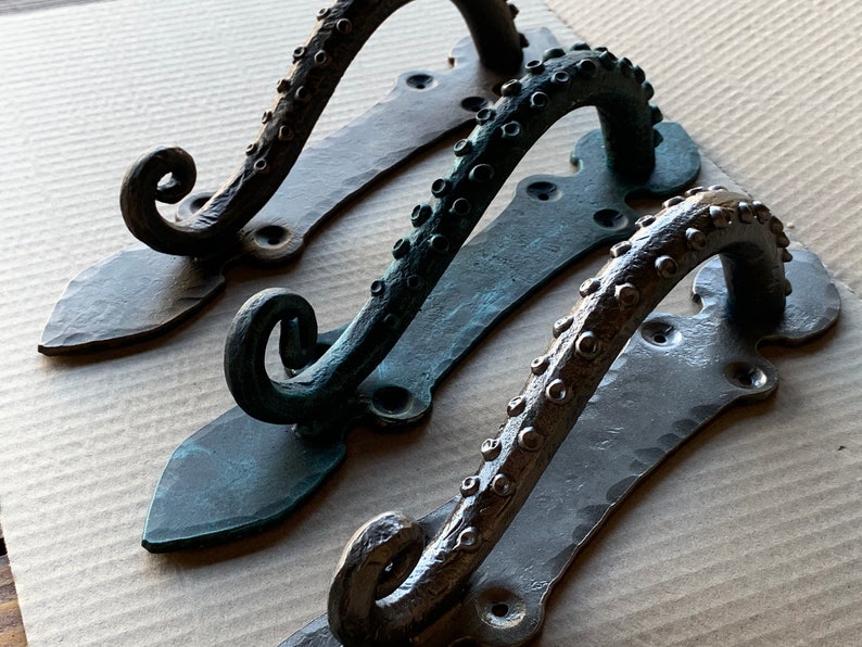May include: Three decorative door handles with an octopus design. The handles are made of metal and have a dark, aged finish. The handles are in different shades of black, green, and brown.