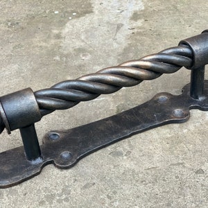 May include: A black metal door handle with a twisted design. The handle has a rounded end and a flat base with a decorative design.