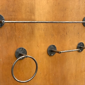 May include: Four metal towel racks mounted on a wood wall. The racks are made of black metal and have a simple, industrial design. Two of the racks are straight bars, and the other two are rings.