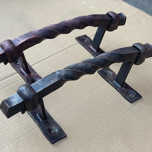Könnte beinhalten: Zwei schwarze Metall-Türgriffe mit einem gedrehten Design. Die Griffe sind auf rechteckigen Metallplatten mit Schrauben montiert.