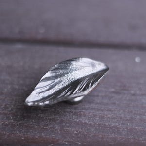 Może przedstawiać: Srebrny klamka do drzwi w kształcie liścia z fakturowaną powierzchnią.