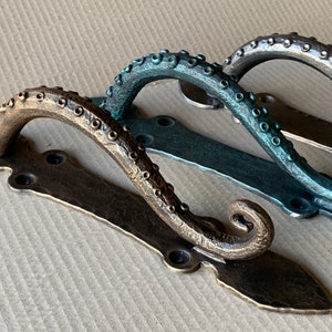 May include: Three octopus-shaped door handles with a decorative, ornate design. The handles are made of metal and are finished in bronze, teal, and silver.