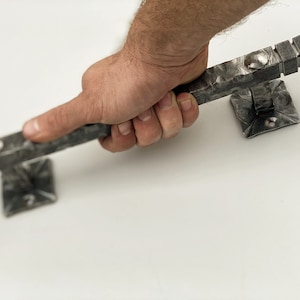 Könnte beinhalten: Eine Hand hält einen silbernen Türgriff aus Metall mit quadratischem Sockel. Der Griff ist strukturiert und hat eine gehämmerte Oberfläche.