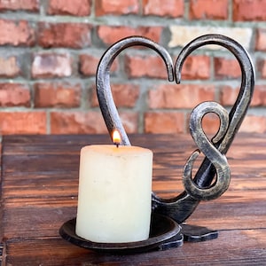 Peut inclure: Un bougeoir en métal noir en forme de cœur avec un symbole d'infini. Une bougie blanche brûle à l'intérieur du bougeoir.