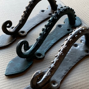 May include: Three decorative door handles featuring an octopus design. The handles are made of metal and have a dark, aged finish. The handles are in different shades of black, green, and brown.