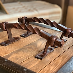 May include: Two rustic, twisted metal door handles with a dark brown finish. The handles are mounted on a wooden surface.