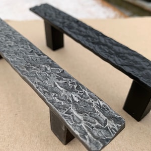 May include: Two cabinet pulls with a textured, hammered finish. One pull is black and the other is silver.