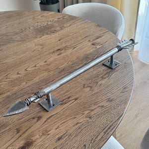 May include: A silver arrow-shaped door pull with a wooden base, mounted on a wooden table.