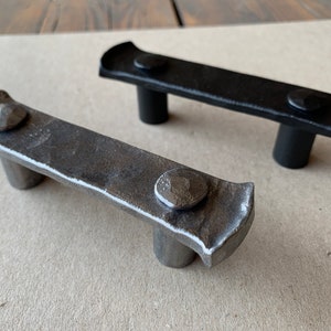 Peut inclure: Deux poignées de tiroir en métal avec une finition martelée. La poignée de gauche est argentée et la poignée de droite est noire.