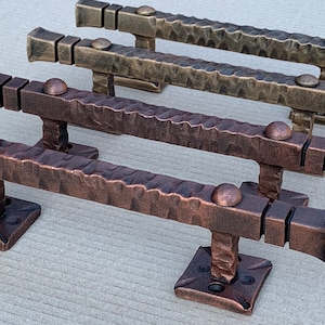 May include: Three rustic iron door handles in different finishes: copper, brass, and antique brass. Each handle has a square base and a rounded knob.