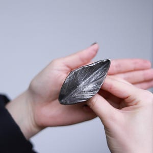 May include: A silver leaf-shaped ring with a textured surface.