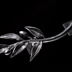 May include: A silver metal olive branch wall mount with a square base. The branch is curved and has leaves and olives.
