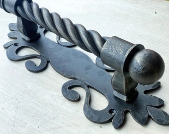 May include: A black metal door handle with a twisted design and ornate scrollwork. The handle is attached to a rectangular plate with a decorative design.