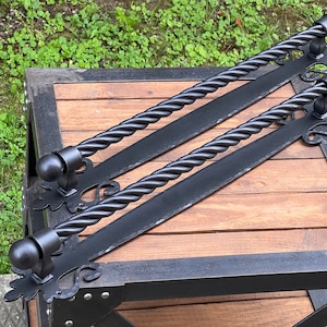 May include: Two black metal door handles with a twisted rope design and ornate scrollwork. The handles are mounted on a wooden surface.