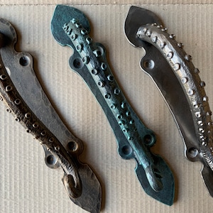 May include: Three decorative door handles in the shape of an octopus tentacle. The handles are made of metal and have a textured surface. The handles are in different colors: bronze, green, and silver.