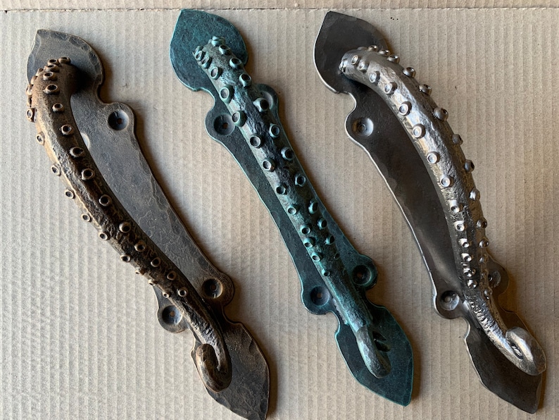May include: Three decorative door handles in the shape of an octopus tentacle. The handles are made of metal and have a textured surface. The handles are in different colors: bronze, green, and silver.