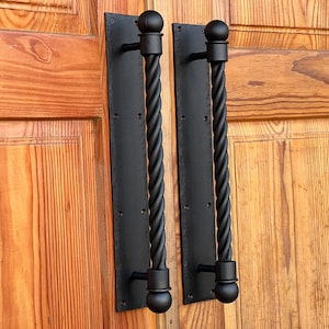 Könnte beinhalten: Zwei schwarze, gedrehte Metall-Türgriffe mit abgerundeten Knöpfen. Die Griffe sind an einer Holztür montiert.