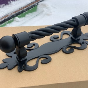 Könnte beinhalten: Schwarzer Türgriff aus Metall mit einem gedrehten Design und dekorativen Schnörkeln.