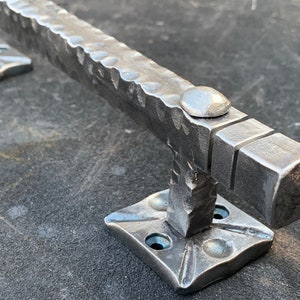 May include: A hammered metal door handle with a square design and a rounded top. The handle is attached to a square base with four screws.