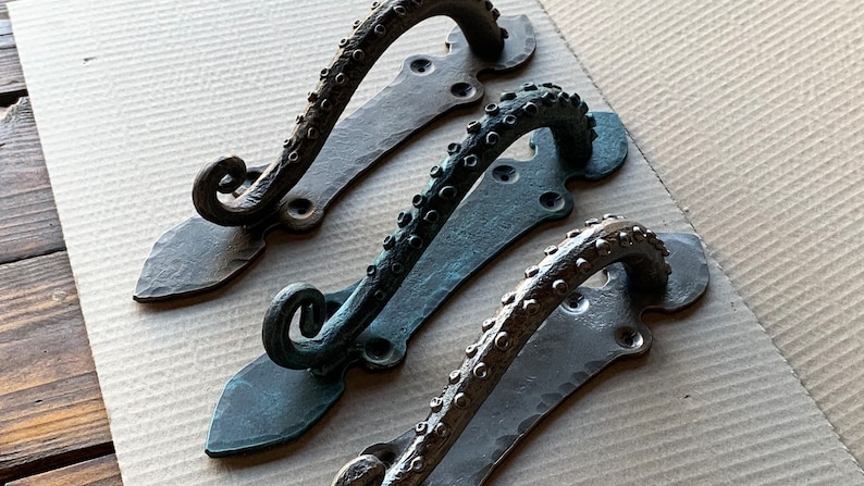 May include: Three octopus-shaped door handles in different finishes: black, bronze, and copper. Each handle has a textured, organic design with a curved shape and a decorative base.