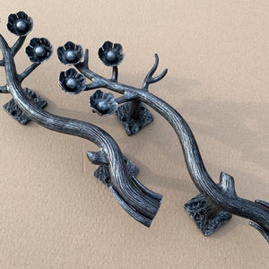 Pode incluir: Um par de puxadores de porta de metal preto em forma de galhos com detalhes de flores estilizadas.