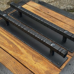 May include: Two black metal door handles with a textured finish, mounted on a wooden surface.