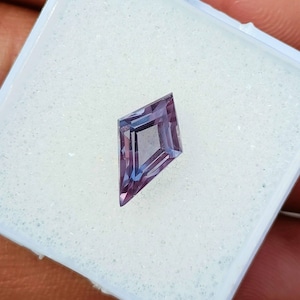 May include: A purple gemstone with a kite-shaped cut, displayed on a white foam background.