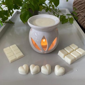 May include: White ceramic wax warmer with a candle inside and a white wax melt bar and heart-shaped wax melts on a white surface.