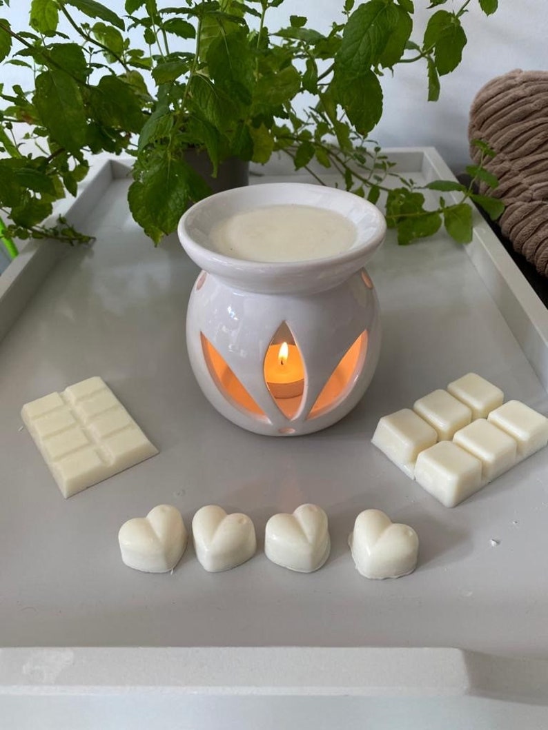 May include: White ceramic wax warmer with a candle inside and a white wax melt bar and heart-shaped wax melts on a white surface.
