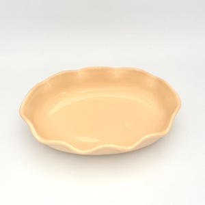May include: A peach-colored ceramic serving dish with a scalloped edge. The shallow, oval-shaped dish has a glossy finish and is set against a white background. This dish is suitable for serving appetizers or desserts.
